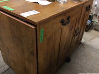 Side view of wooden craft table showing pull-out extension panel and cabinet door with metal handle, on caster wheels.