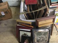 Bins containing assorted photo frames in different sizes and finishes including wood and metal frames on floor.