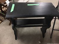 Front and side view of the rectangular black painted wood magazine rack table, showing the overall structure and shelf space.