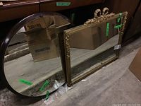 Round wooden framed mirror and rectangular ornate gold framed mirror leaning against a dresser.