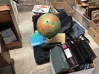Photo of vintage globe, various office supplies including binders, computer bags, file folders, metal cash box, plastic envelope pouches, and blank paper notebooks on floor.