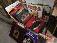 Multiple vinyl record albums stacked in box showing varied album covers including a piano-themed album and Frankie Valli and The Four Seasons album