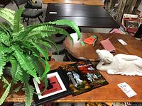 Full view of the lot items on wooden table: reclining Buddha statue, faux fern plant, and three-panel Asian themed wall art