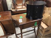 Photo of vintage wooden table with a curved front and turned front legs, black jewelry box on top, showing sides and surface wear.
