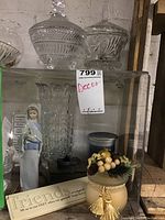 Shelf display containing Lladro figurine, crystal candy dishes, decorative vase, pottery butter dish, candle, and motivational plaque.