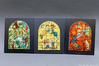 Three wall plaques depicting Marc Chagall stained glass window replicas arranged side by side on a surface.