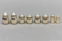 Front view of four pairs of sterling silver salt and pepper shakers in a row, varying slightly in size and shape, on gray background