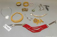 Full lot overview of assorted costume jewelry on grey surface including necklaces, bangles, bracelets, and rings