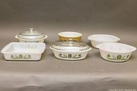 Photo showing a variety of vintage casserole dishes with glass lids including Glasbake Green Daisies pattern dishes in various shapes and sizes.