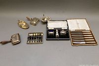 Full view of lot showing all items arranged in a line: salt cellars, spoons, cigarette case, knives, and small box.