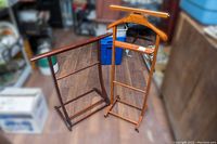 Two vintage wooden valet stands, one upright with wide hanger and attached towel rack, the other lying on its side showing base and frame details.