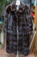 Full front view of the long dark brown mink and leather fur coat on a hanger, showing full length, collar, and button closure.