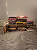 Stack of various books arranged on floor including some with visible spines showing authors and titles