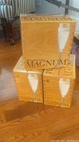 Boxes labeled 'MAGNUM' with images of champagne flutes, stacked on wooden floor.