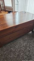 Photo showing the side of the rectangular wooden coffee table with a large bottom drawer and round wooden knobs, as well as signs of scratching and dings on the wood finish.