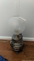 Full view of the metal lamp showing the etched glass globe shade and cylindrical chimney
