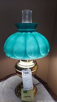 Full view of table lamp illuminated with teal glass dome shade and brass base.