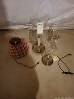 View of two brass tone hurricane lamps with glass chimneys and checkered fabric lamp shade on floor.