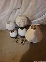 Photo showing three vintage lamps including two with glass globes and one with pleated fabric shade, cords and switches visible