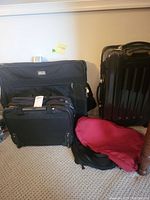 Front view of all luggage items together including standing black ridged hard suitcase, two black duffel bags, maroon garment bag