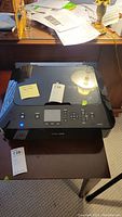Full view of the Canon PIXMA MG5420 printer showing glossy black finish, touchscreen, control buttons, and paper tray open.