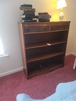 Front view of a wooden shelf with two drawers and decorative trim showing scratches and wear.