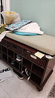 Side view showing beige cushion atop the wooden shoe rack and three woven baskets in upper cubbies.