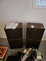 Full view of two Sony floor speakers standing side by side against a wall, with power strips and cables visible in front of them.