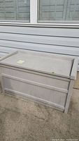 Full view of beige plastic deck box closed, outdoor placement, surface dusty and dirty.