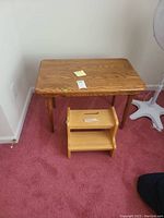 View of wooden table next to two-step stool on carpeted floor