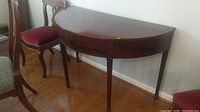 Front view of demi lune wood table showing half-moon top and legs with scratches and watermarks.