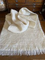 Full view of butter cream color mohair scarf with fringe on both ends laid on wooden surface, showing texture and draping.
