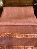 Full view of folded coral wool blanket showing satin binding on edge.