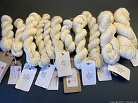 Overview of 11 skeins of natural fiber yarn in neutral shades with original tags attached, various compositions of cashmere, silk, and merino wool blends.