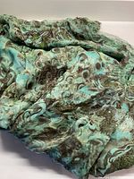 Close-up image showing lightweight chiffon fabric with turquoise, grey, and blue abstract pattern resembling peacock feathers.