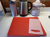 Electric can opener, electric teapot, electric juicer, and two synthetic cutting boards on countertop.