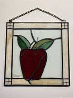 Full view of square stained glass panel showing red apple with green and yellow leaves on clear glass background with cream border and hanging chain