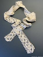 Full length of cream antique lace trim rolled on black background showing scalloped edges and intricate openwork pattern.