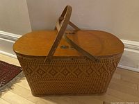 Side view of the large oval wicker basket showing the woven diamond pattern and the attached wooden handle in upright position.