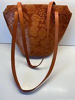 Front view of the pumpkin-colored genuine leather shoulder bag embossed with fruits and leaves showing full bag and shoulder straps.