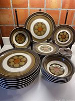 View of full dish set with plates, bowls, and sugar bowl arranged on display stand and flat surface, showing pattern and colors