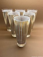 Front view showing six frosted glass tumblers with vertical gold convex lines.