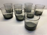 Overview of 8 smoky grey lowball glasses arranged in two rows on a white surface showcasing the size and color.