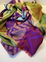 Close-up image showing colorful geometric patterns in green, purple, blue, and red with fringed edges on the soft fabric.