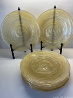 Front view showing three of the amber-colored glass plates upright and stacked plates in front, highlighting swirling patterns and transparent amber glass.