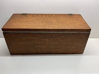 Front view of the oak wooden container with closed hinged lid, showing wood grain and rectangular shape