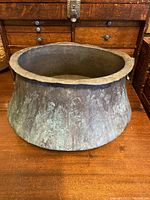 Front view of a very old, rustic copper cauldron with a wide base and narrower opening, showing heavy oxidation and aged patina.