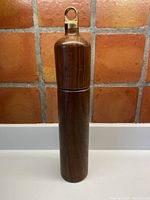 Full view of tall walnut pepper grinder with brass ring top against tiled wall background
