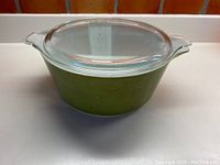 Full view of the round avocado green Pyrex casserole dish with clear lid.