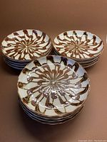 Twelve stacked ceramic luncheon plates showing cinnamon swirl pattern on a pale cream grey background, arranged in three stacks.